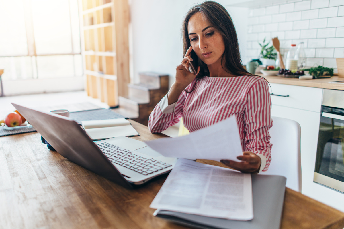 Woman working on laptop, talking on phone and reading documents